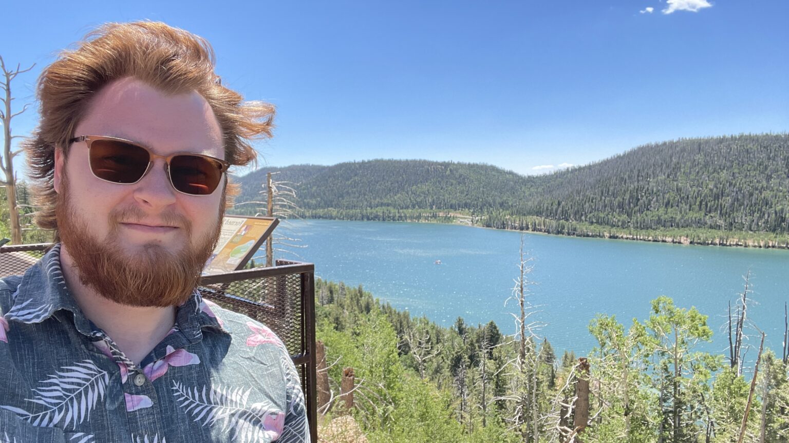 Jared smiling at a lake, Hawaiian shirt and sunglasses